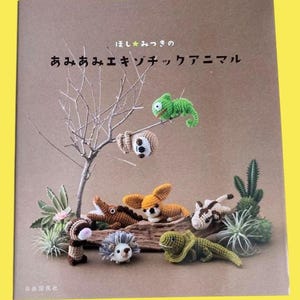 May include: A book cover featuring a collection of crocheted exotic animals, including a chameleon, sloth, and hedgehog. The title is in Japanese. The background is a neutral brown with a yellow border.