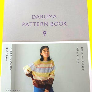 May include: A book cover with the text "DARUMA PATTERN BOOK 9" in purple. Below, a woman models a striped sweater in yellow, grey, and burgundy. The book cover also includes Japanese text and the Daruma logo.