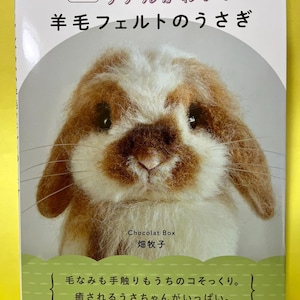 May include: A softcover book featuring a needle-felted brown and white rabbit on the cover. The Japanese text reads: 改訂新版 リアルかわいい 羊毛フェルトのうさぎ, Chocolat Box 畑牧子, 毛なみも手触りもうちのコそっくり。 癒されるうさちゃんがいっぱい。 河出書房新社.
