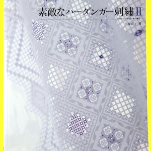 Peut inclure: Couverture de livre avec le titre "FINE HARDANGER EMBROIDERY" et du texte japonais. La couverture présente un gros plan d'un tissu brodé blanc et lavande avec des motifs géométriques. Le livre a une bordure jaune.