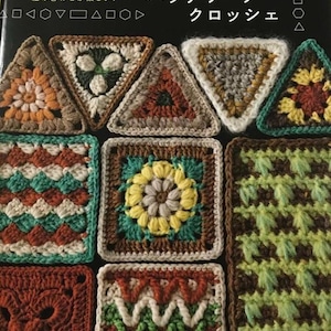 以下が含まれることがあります： 様々な色のパッチワークかぎ針編みのデザインが特徴の書籍の表紙。茶色、緑、黄色、白の色合いの三角形と正方形のかぎ針編みパターンが含まれています。日本語のテキストが表紙の上部と側面に表示されています。