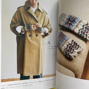 May include: A pair of fingerless knit gloves featuring a detailed Nordic-inspired pattern in cream, black, and blue. The gloves are shown being worn with a tan double-breasted trench coat and also displayed separately on a textured surface.