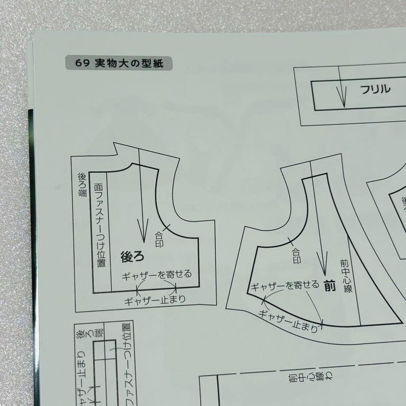 Op de afbeelding: Een pagina uit een naaipatronenboek met Japanse tekst. De pagina bevat diagrammen van kledingstukken, waaronder een voor- en achterpand, met labels en markeringen. De tekst bevat zinnen als "franje" en "verzamelen".