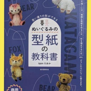 以下が含まれることがあります： 青い背景の表紙には、ぬいぐるみと日本語のテキストが描かれています。「Nui-gurumi no Katagami no Kyokasho」というタイトルが中央に配置され、キツネ、クマ、犬のぬいぐるみが描かれています。表紙には黄色の縁取りがあります。