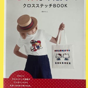 以下が含まれることがあります： ハローキティとパティ＆ジミーのクロスステッチBOOKの表紙。赤い背景に白い文字とイラストが描かれています。白いTシャツと麦わら帽子をかぶった人が写っており、Hello Kittyのクロスステッチが施された白いトートバッグを持っています。