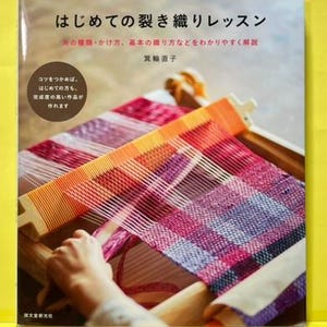 May include: A book cover titled "はじめての裂き織りレッスン" featuring a wooden loom with a colorful, multi-textured fabric in shades of pink, purple, and orange being woven. The cover includes Japanese text and a circular callout box with text.