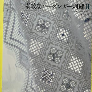 May include: A softcover book titled Fine Hardanger Embroidery with the Japanese text 素敵なハーダンガー刺繍II on the cover. The cover features a detailed white-on-white geometric Hardanger embroidery pattern with intricate cutwork and needlework.