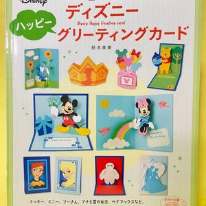 以下が含まれることがあります： ディズニーハッピーグリーティングカードというタイトルのソフトカバー本。ライトグリーンの表紙には、ミッキーマウス、ミニーマウス、くまのプーさん、ベイマックスなどのカラフルなポップアップカードのデザインが多数掲載されており、日本語のテキストとディズニーのロゴが記載されています。