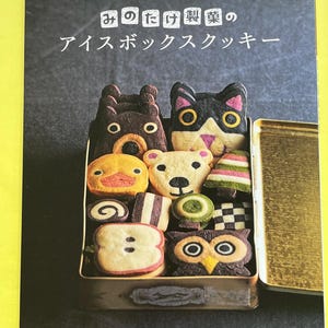 May include: A cookbook titled "Mino Take Seika's Icebox Cookies" with a box of animal-shaped cookies. The cookies include a bear, cat, duck, owl, and other designs. The book cover is dark gray with Japanese text.