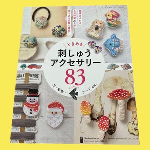 May include: A book cover featuring embroidered accessories. The cover displays various handmade items, including floral hair accessories, brooches, and mushroom designs. The title reads "Embroidery Accessories 83" in Japanese, with additional text and illustrations.