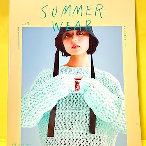 Peut inclure: Un livre à couverture souple intitulé SUMMER WEAR vol. 3 Hand Knitting Recipe Book. La couverture montre une personne portant un chapeau bob sombre avec de longs liens noirs et un pull à manches longues en tricot ajouré vert menthe clair.
