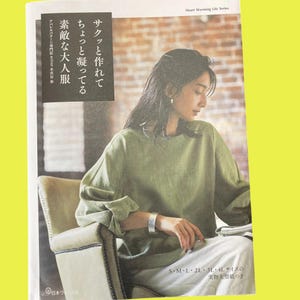 以下が含まれることがあります： 緑色の長袖シャツと白いパンツを着た女性が写っている雑誌のページ。ページには日本語の文字と「Heart Warming Life Series」という文字が書かれています。雑誌には「S-M-L 2L 3L 4L sizes」という文字も書かれています。