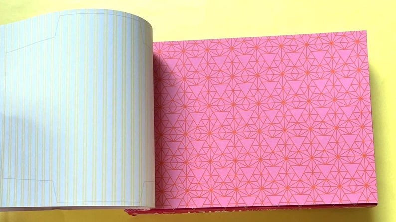 Puede incluir: Cuaderno abierto con p&aacute;ginas que muestran un patr&oacute;n geom&eacute;trico rosa y p&aacute;ginas rayadas. El patr&oacute;n rosa presenta un dise&ntilde;o repetitivo de tri&aacute;ngulos y l&iacute;neas en un tono m&aacute;s claro de rosa. Las p&aacute;ginas rayadas tienen l&iacute;neas verticales amarillas.