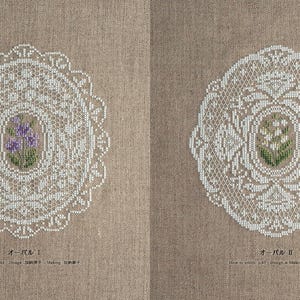 Op de afbeelding: Twee gedetailleerde witte kanten doilies met bloemmotieven in het midden, op een beige stoffen achtergrond. E&eacute;n doily heeft paarse bloemen, de andere witte. De ovale doilies hebben ingewikkelde patronen.