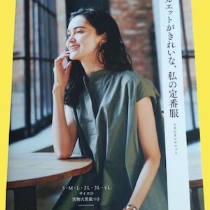 May include: A woman in a green dress smiles, resting on a wooden table. The image is from a magazine with Japanese text, including "Heart Warming Life Series" and "S M L 2L 3L 4L". The text also mentions "Silhouette" and "My favourite clothes".