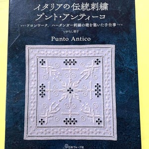 Peut inclure: Un livre en japonais, intitulé "Punto Antico", présentant une broderie blanche détaillée sur la couverture. Le motif comprend des motifs floraux et géométriques. La couverture du livre est bleu foncé avec du texte japonais et le logo de l'éditeur.