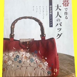 Könnte beinhalten: Ein Buchcover mit einer rot-beigen Handtasche mit Bambusgriff. Die Tasche ist mit floralen Mustern in Blau, Weiß und Orange verziert. Japanischer Text ist sichtbar, darunter "Erwachsenen-Taschen" und "Taschen mit Obi herstellen".