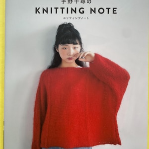May include: A softcover book titled "宇野千尋の KNITTING NOTE ニッティングノート" featuring a cover photograph of a person wearing a bright red, long-sleeved, fuzzy knit sweater and blue denim jeans against a plain, light gray background.