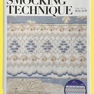 May include: A book cover displaying the title "SMOCKING TECHNIQUE" with Japanese text. The cover showcases intricate embroidery in white, blue, and beige, demonstrating different smocking patterns. A small inset with more smocking designs is also included.