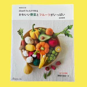 以下が含まれることがあります： フェルトで作られた野菜と果物がたくさん入った木製のボウルが特徴の書籍の表紙。カボチャ、アボカド、キウイなど。本のタイトルは日本語で、フェルトの野菜や果物の作り方について書かれています。