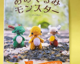 以下が含まれることがあります： 「手のひらサイズのあみぐるみモンスター」というタイトルの書籍の表紙。緑、黄色、ベージュの3体の小さな編みぐるみのモンスターが写っており、左下にはマンドラゴラの編みぐるみがある。表紙には日本語のタイトルと、掲載されているクリーチャーの名前のリストが記載されている。