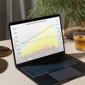 Könnte beinhalten: Ein schwarzer Laptop zeigt ein Finanzdiagramm mit der Aufschrift "EINKOMMEN & INVESTITIONEN - NÄCHSTE 25 JAHRE". Das Diagramm zeigt Einkommen und Investitionen über 25 Jahre, mit gelben und grünen Balken. Ein Glas bernsteinfarbener Flüssigkeit und eine dekorative Pflanze sind zu sehen.