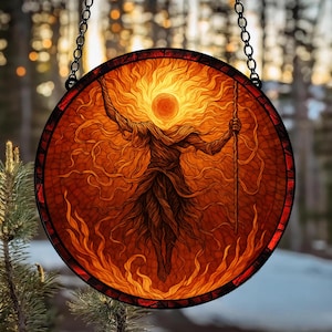 May include: Round stained glass panel featuring a fiery figure with outstretched arms and a staff. The artwork is predominantly orange and red, with a sun-like element at the top. The panel is framed with a dark border and suspended by a chain.