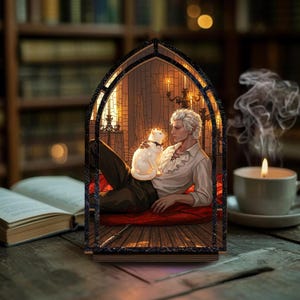 Puede incluir: Una pieza de arte decorativa de madera que representa a un hombre con cabello blanco y un gato blanco. El hombre está reclinado sobre un cojín rojo dentro de un marco de estilo vidriera. Velas y una estantería están en el fondo.