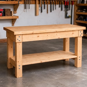 May include: A rectangular wooden workbench featuring a thick top surface and a lower storage shelf. The structure is supported by four sturdy legs, with metal bolts visible at each corner joint, showcasing a natural light brown wood grain finish.
