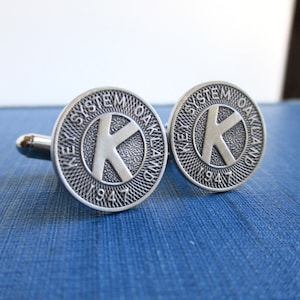 May include: A pair of silver cufflinks featuring the Key System Oakland logo with the year 1947.