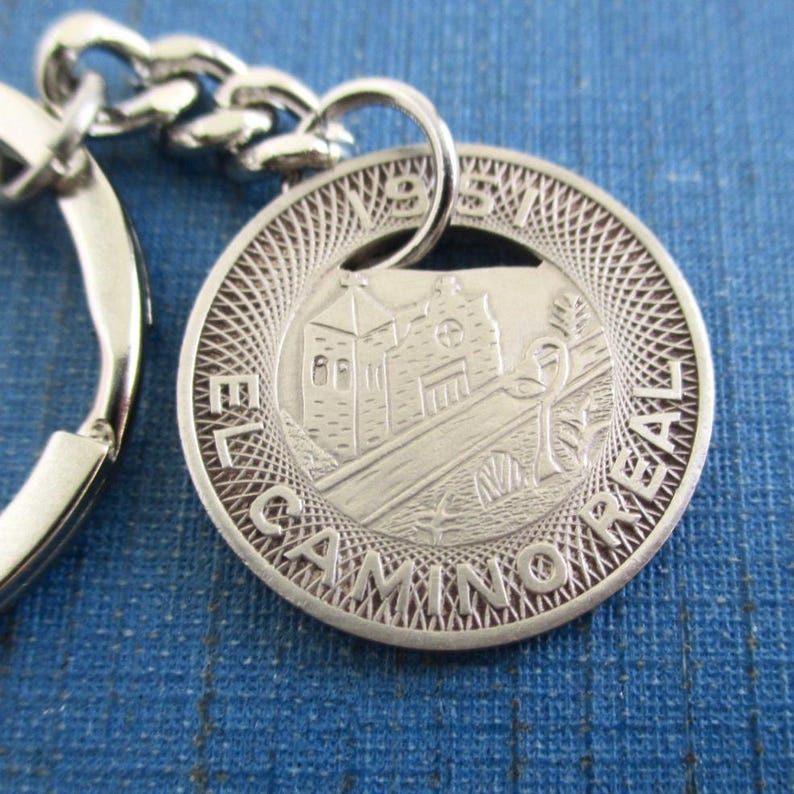 May include: Silver-colored keychain with a round pendant featuring a detailed engraving of a building, bridge, and text "EL CAMINO REAL 1951". The keychain includes a chain and a key ring.
