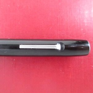 May include: Close-up of a black pen with a silver clip and a rounded end. The pen's body is glossy, and the clip is a thin, rectangular bar. The pen is set against a red background.