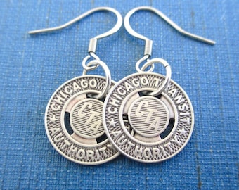 May include: A pair of silver-toned metal drop earrings featuring circular charms. Each charm is embossed with the text CHICAGO TRANSIT AUTHORITY and CTA in the center, suspended from curved metal ear wires for pierced ears.