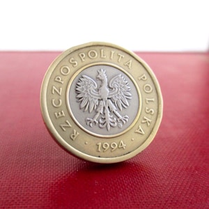 May include: A Polish coin from 1994, featuring a silver eagle emblem at the center, surrounded by text in Polish. The coin has a gold-colored outer ring and is set against a red background.