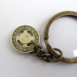 May include: A brass keychain with a round token featuring the text "Duke Power Company" and a star. The token has a large "D" in the center.