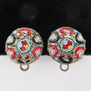 May include: A pair of vintage earrings with a round, multi-colored mosaic design. The earrings are made of silver metal and have a small loop at the bottom.