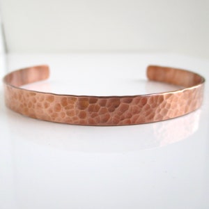 May include: A hammered copper bracelet with a smooth, polished finish. The bracelet is a simple, minimalist design and is made of a single piece of metal.