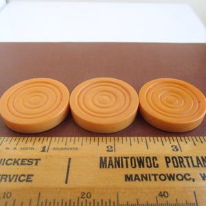 May include: Three orange plastic game pieces with a concentric circle design. The pieces are about 1 inch in diameter.