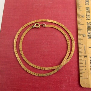 May include: A gold chain necklace with a box clasp. The chain is made of small, flat, linked squares. The necklace is about 18 inches long.