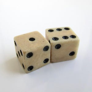 Puede incluir: Dos dados de color marfil con puntos negros. Un dado muestra tres puntos, el otro seis. Los dados están sobre un fondo blanco. Estos dados son adecuados para juegos de mesa.