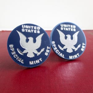 May include: A pair of blue and silver cufflinks featuring the United States Special Mint Set 1987 design. The cufflinks are round and feature a silver eagle with a blue background.