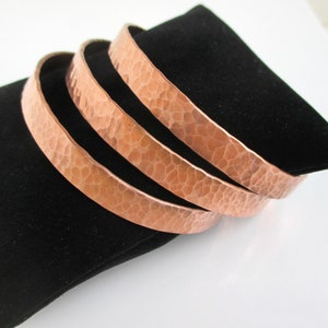 May include: Three copper bracelets with a hammered texture. The bracelets are stacked on top of each other.