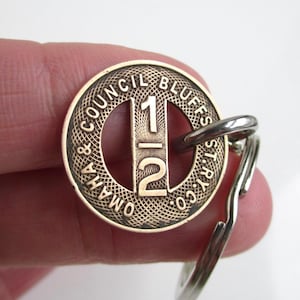 May include: A vintage Council Bluffs St. Ry. Co. token with the number 12 in the center. The token is made of brass and attached to a silver-colored keyring.