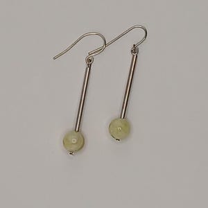 May include: A pair of silver earrings with a light green bead at the bottom of each earring.
