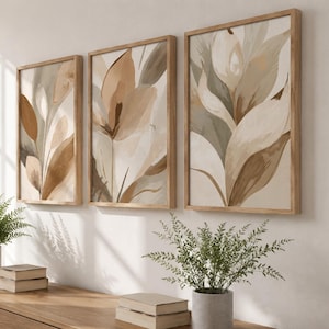 Könnte beinhalten: Ein Set aus drei rechteckigen Wandbildern mit abstrakten botanischen Illustrationen in Beige-, Creme- und gedämpften Salbeigrüntönen. Jeder Druck ist in einem hellen Holzrahmen gefasst und zeigt fließende, organische Blattformen.