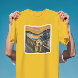 Pode incluir: Camiseta amarela com uma paródia de "O Grito" de Edvard Munch. O gráfico mostra um personagem de desenho animado no estilo da obra original. A camiseta é exibida em um fundo azul.