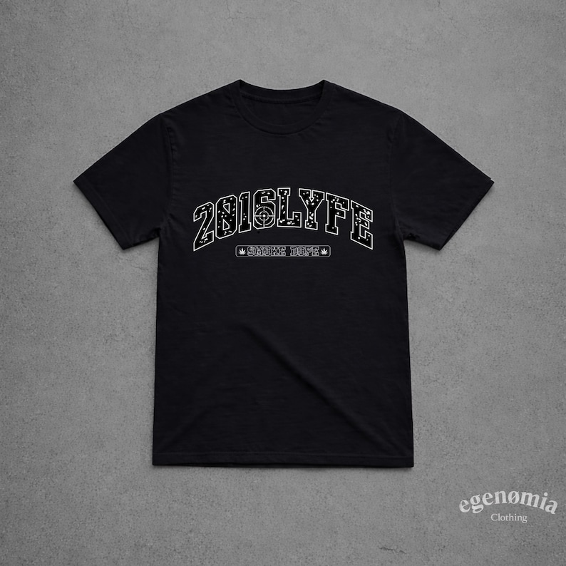 K&ouml;nnte beinhalten: Schwarzes T-Shirt mit dem wei&szlig;en Schriftzug "2016LYFE" in einer Schriftart im College-Stil. Darunter steht der Schriftzug "SMOKE DAPE" in kleinerer Schrift, flankiert von Stern- und Blattmotiven. Das T-Shirt ist aus weichem Material.