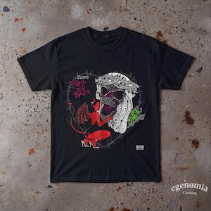 Könnte beinhalten: Ein schwarzes Kurzarm-T-Shirt mit einem Grafikdruck eines Schädels mit Dornenkrone, einer roten Teufelsfigur und einer kleinen grünen Kreatur. Der Text lautet "Encore" und "REST IN BASS" in Pink, umrahmt von einem Herz aus Stacheldraht.