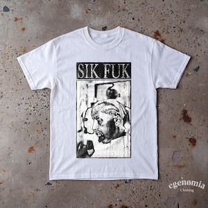 Könnte beinhalten: Ein weißes T-Shirt mit kurzen Ärmeln und einer schwarz-weißen rechteckigen Grafik auf der Brust. Die Grafik zeigt den Text SIK FUK über einer detaillierten Skizze einer Person im Profil, die einen Lorbeerkranz trägt, in einem tintenartigen Stil.