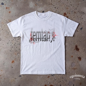 May include: A white short-sleeve t-shirt featuring a black graphic print with the text femtanyl. The design includes a stylised character illustration, red circular accents, and small text details layered over a blurred black background element.